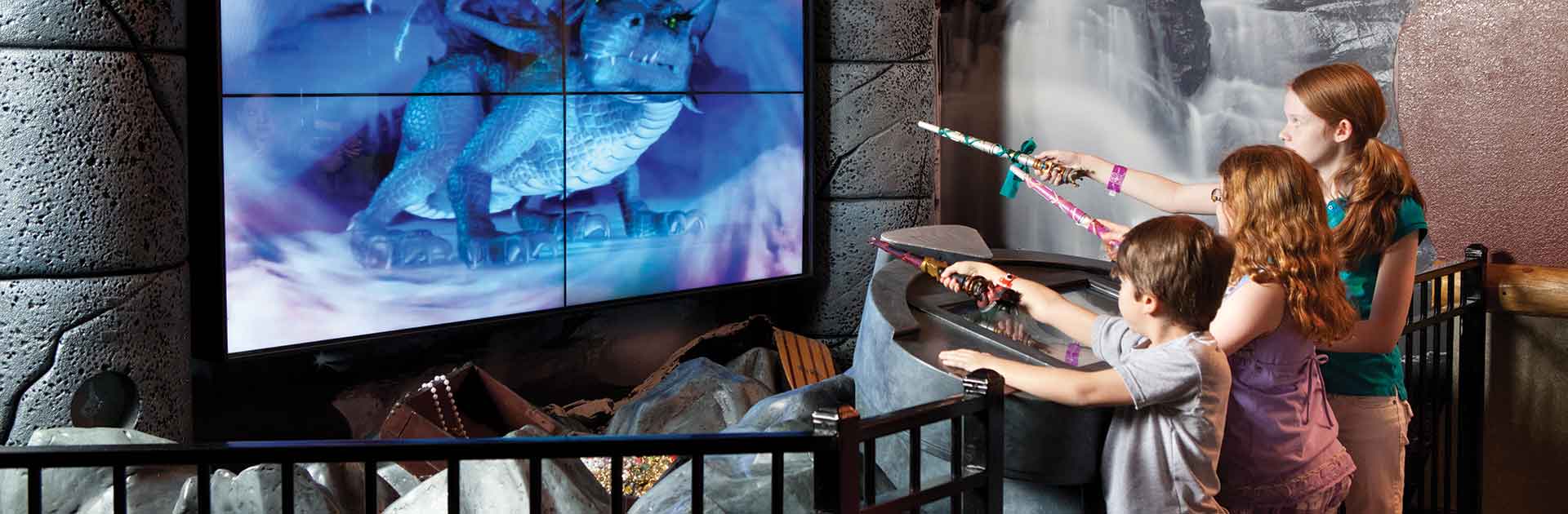 Two kids holding a wand watch a MagiQuest screen